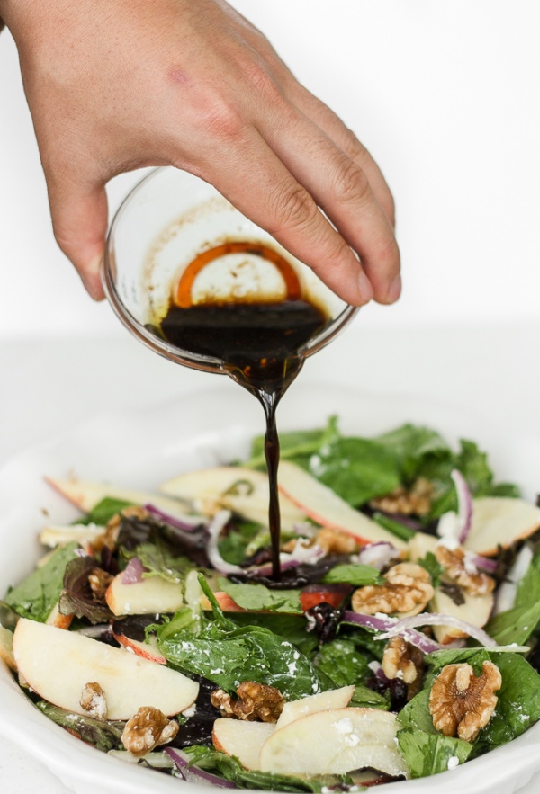 apple walnut salad with vinaigrette being poured over top.